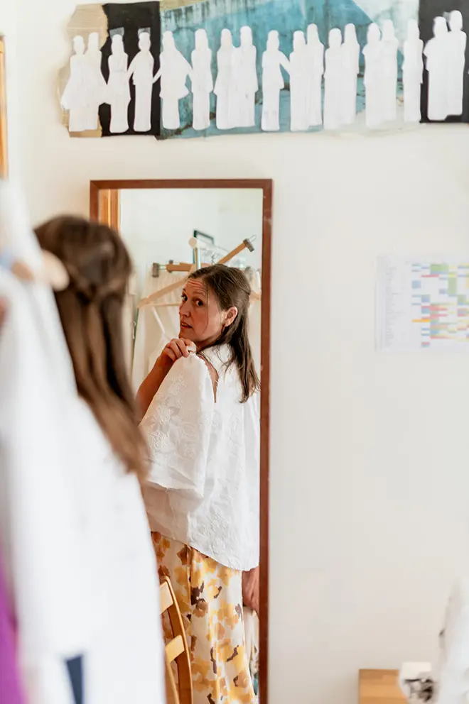 Hanna Westergren på RAORI Slow Fashion står framför en spegel och måttar ett tygstycke till en jacka hon håller på att sy.