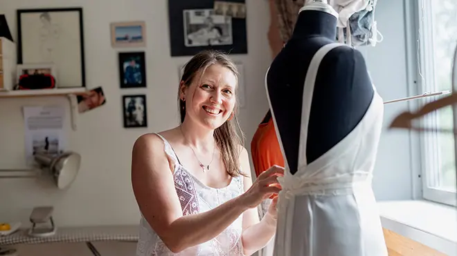 Hanna Westergren på RAORI Slow Fashion står och syr på bakdelen av en klänning som sitter på en provdocka.
